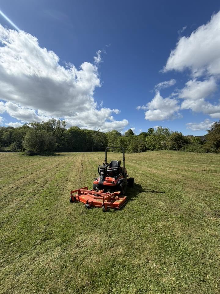 Ride-on mower cutting open grassland on a grounds maintenance contract